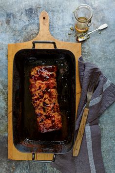 a piece of meat in a pan next to a glass of beer and utensils