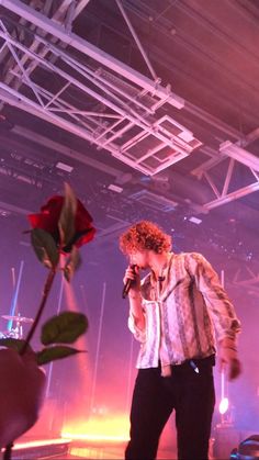 a man holding a microphone while standing next to a red rose in front of him