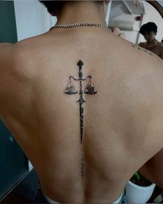 the back of a woman with a tattoo on her shoulder and scales in front of her