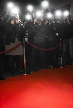 a man in black jacket standing next to a red carpet with cameras on his head