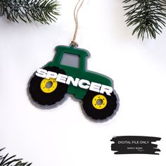 a green tractor ornament hanging from a christmas tree with the word spencer on it