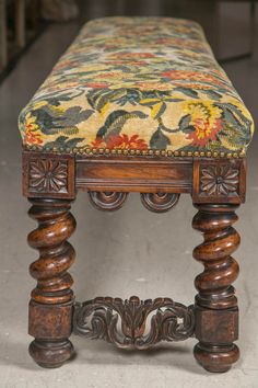 an old wooden bench with a floral upholstered seat and foot rest on the floor