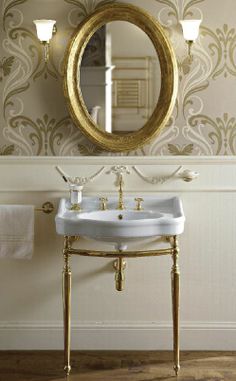 a white sink sitting under a mirror next to a gold framed mirror on a wall