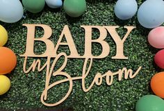 a baby in bloom sign surrounded by balloons and fake grass at an outdoor birthday party