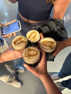 four people are holding up their cell phones and drinking some coffee with frothy liquid on them