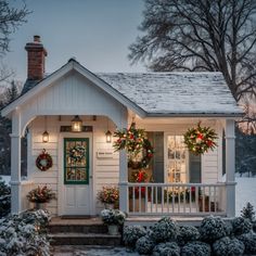 a white house decorated for christmas with wreaths on the front porch and lights on the door