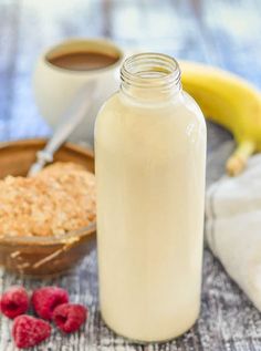 a glass bottle filled with milk next to raspberries and a bowl of oatmeal