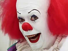 a close up of a person wearing a clown mask with red hair and white makeup