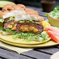 a hamburger with lettuce, tomato and other vegetables on a yellow plate next to watermelon wedges