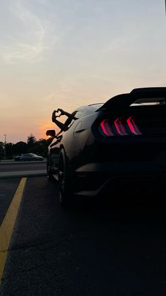 a black sports car parked on the side of the road with its lights on at sunset