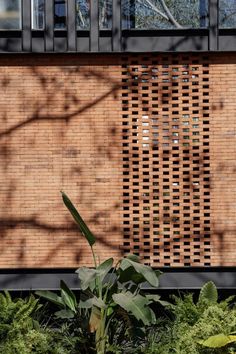 the side of a brick building with plants in front of it and trees on the other side