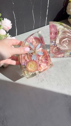 a woman's hand reaching for a flower in a small glass container on top of a table