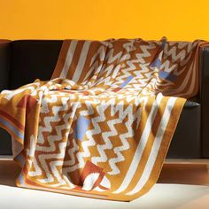 an orange and white blanket sitting on top of a couch next to a black chair