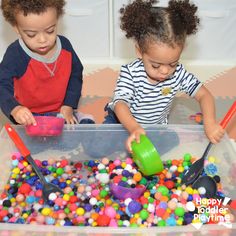 two young children playing in a plastic container filled with colored balls and spoons on the floor