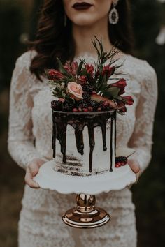 a woman holding a cake with flowers on top and chocolate dripping down the side in front of her face