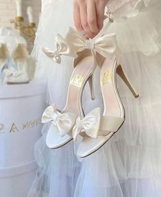 a close up of a person holding a pair of high heeled shoes with bows