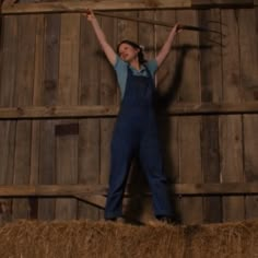 a woman standing on top of a hay bale in front of a wooden wall