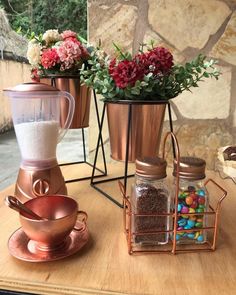 a wooden table topped with copper cups filled with candy and flowers next to a grinder