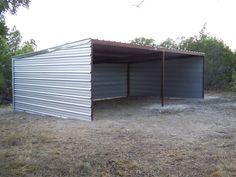 two metal garages sitting in the middle of a dry grass field with trees behind them