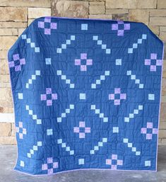 a blue and purple quilt on display in front of a brick wall with bricks behind it