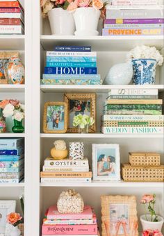 a white bookcase filled with lots of books next to vases and flowers on top of each shelf