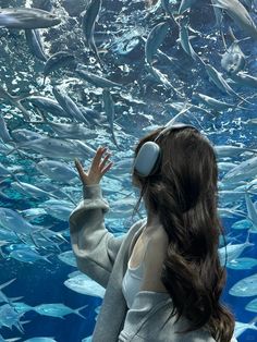 a woman wearing headphones standing in front of a large amount of fish swimming under water