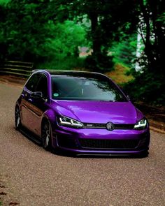 a purple car parked on the side of a road next to some trees and bushes