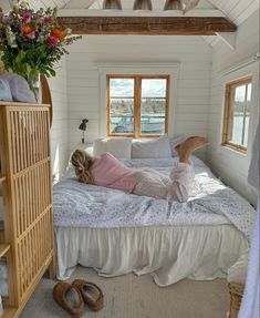 a woman laying on top of a white bed in a bedroom next to a window