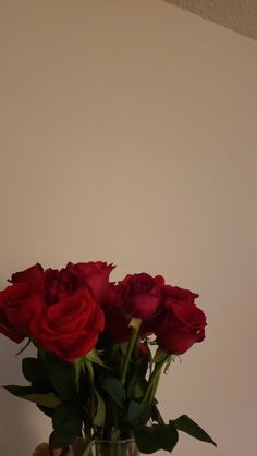 a vase filled with red roses sitting on top of a wooden table next to a white wall