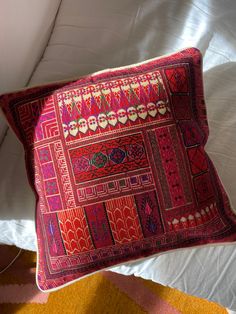 a red pillow sitting on top of a bed next to a yellow rug and white sheets