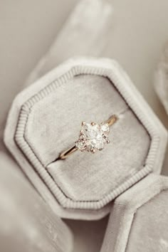 an engagement ring with a diamond sits in a velvet box, surrounded by other jewelry items