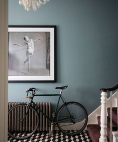 a bicycle parked next to a painting on the wall in a room with blue walls and black and white checkered flooring