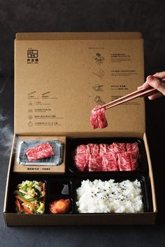 someone is holding chopsticks over some meat in a box with rice and broccoli