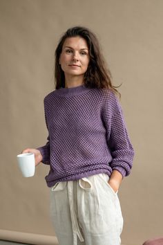 a woman is holding a coffee cup in her hand and wearing a purple knitted sweater