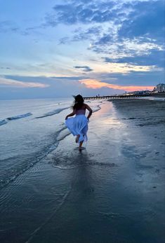 a woman in a white dress is running on the beach at sunset with her hair blowing in the wind