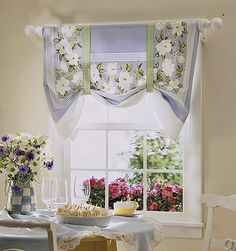 two vases with flowers sit on a table in front of a window that has sheer curtains