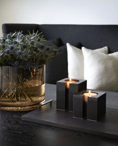 three candles are sitting on a tray next to a vase with some flowers in it