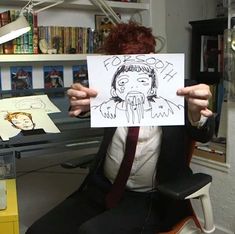 a person sitting in a chair holding up a paper with a drawing of a man's face on it