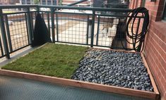 a balcony area with grass and rocks in the ground next to a metal fence on top of a brick building