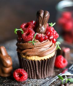 a cupcake with chocolate frosting and raspberries in the shape of rabbits