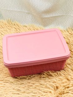 a pink lunch box sitting on top of a fluffy rug next to a white blanket