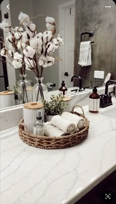 a bathroom counter topped with a basket filled with cotton flowers and other items next to a mirror