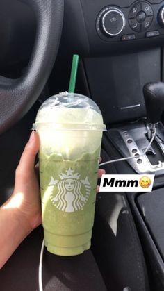 a person holding a starbucks drink in their hand while sitting in the driver's seat of a car