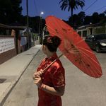 a woman in a red dress holding an umbrella on the side of the road at night