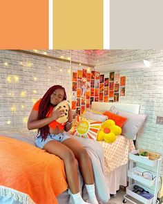 a woman sitting on top of a bed next to a white brick wall with orange and yellow accents