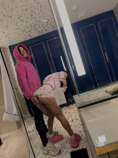 a woman standing in front of a bathroom mirror next to a man taking a selfie