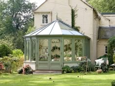 a gazebo in front of a house with lots of greenery on the lawn