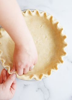 a person is placing an uncooked pie crust on top of the pie pan