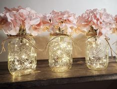 three mason jars filled with pink flowers and string lights