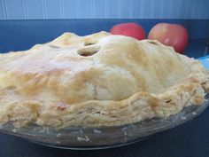 a pie sitting on top of a glass plate next to two red apples in the background